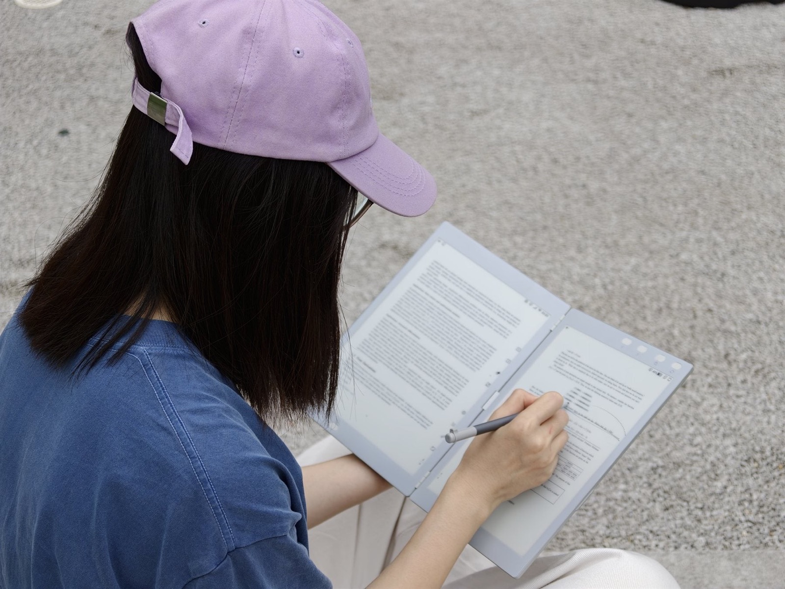 Une personne lit sur un écran E Ink de l'InkLeaf et écrit au stylet sur le second écran du carnet numérique pliable
