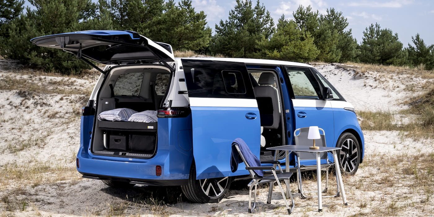 Le van électrique Volkswagen ID. California Cruise, hayon et porte latérale ouverts, aménagé avec table et chaises de camping sur le sable