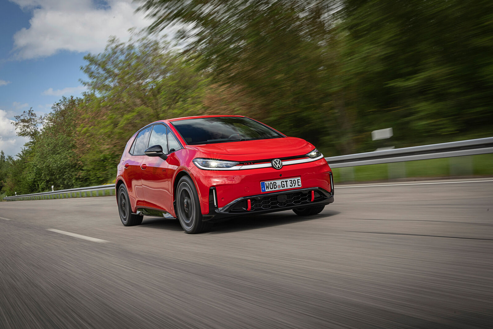 La Volkswagen ID.3 GTI rouge en vue trois quarts avant, roulant sur route, badge GTI et logo Volkswagen visibles