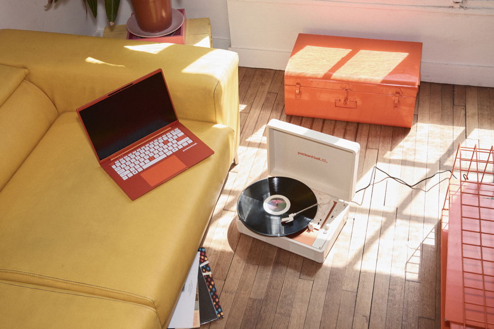 Ordinateur portable Packard Bell DotBook orange posé sur un canapé, à côté d'une platine vinyle DotLoop