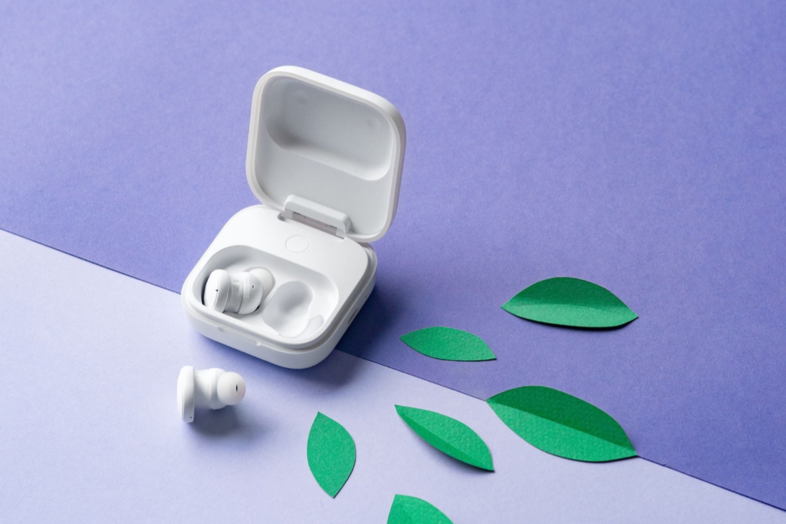 Les écouteurs sans fil Fairphone Fairbuds 2 en blanc, un écouteur à tige posé devant leur boîtier de recharge ouvert