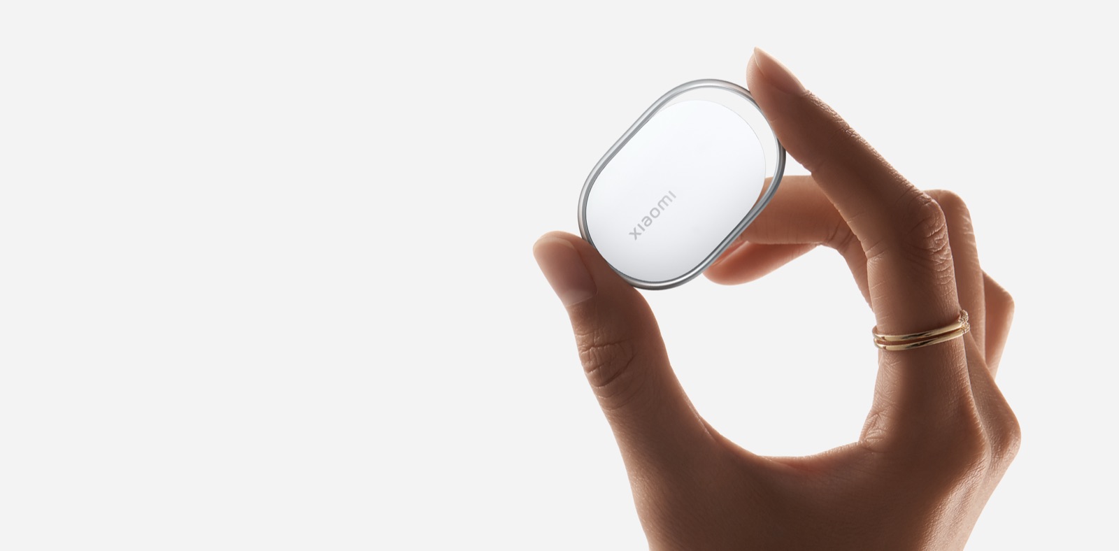 Une main tient le traqueur Bluetooth Xiaomi Tag, un petit boîtier blanc de forme ovale