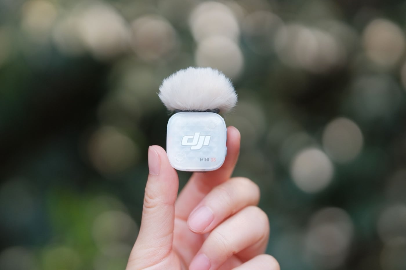 Le micro-cravate sans fil DJI Mic Mini 2S tenu entre deux doigts, avec sa bonnette anti-vent