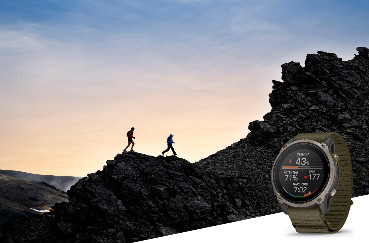 Montre Garmin Enduro 4 au bracelet textile kaki affichant l'endurance, devant un decor de trail en montagne