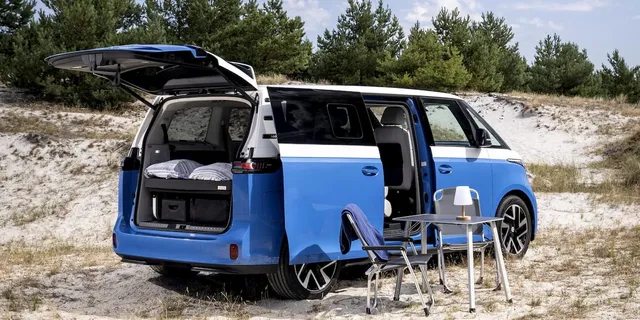 Le van électrique Volkswagen ID. California Cruise, hayon et porte latérale ouverts, aménagé avec table et chaises de camping sur le sable