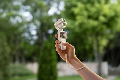La caméra de poche DJI Osmo Pocket 4P en coloris Blanc perle, tenue à la main, nacelle et double objectif visibles